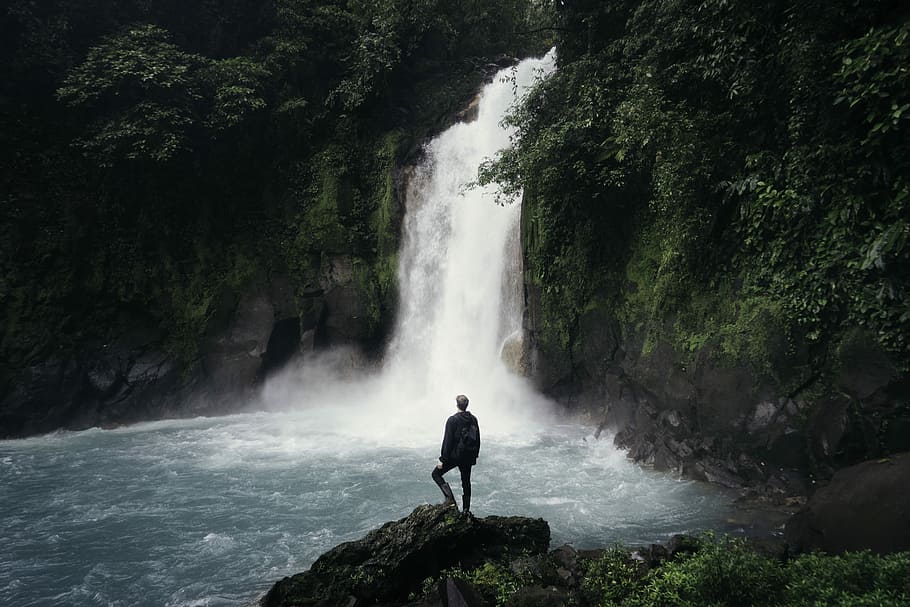man standing on cliff near falls, man standing near waterfalls during daytime HD wallpaper