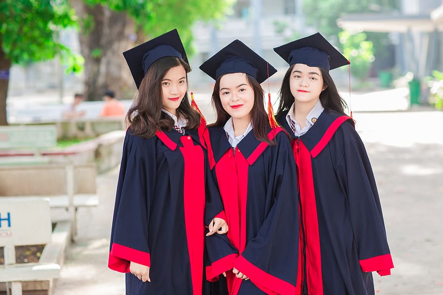 three women wearing black-and-red academic dresses outdoors, friend