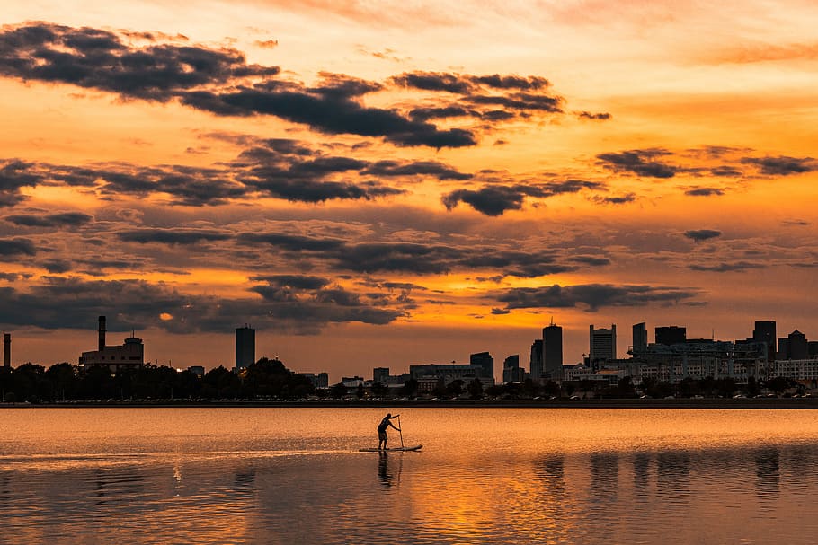 landscape photography of silhouette of man on boat near city buildings, silhouette of man in black boat during sunset HD wallpaper