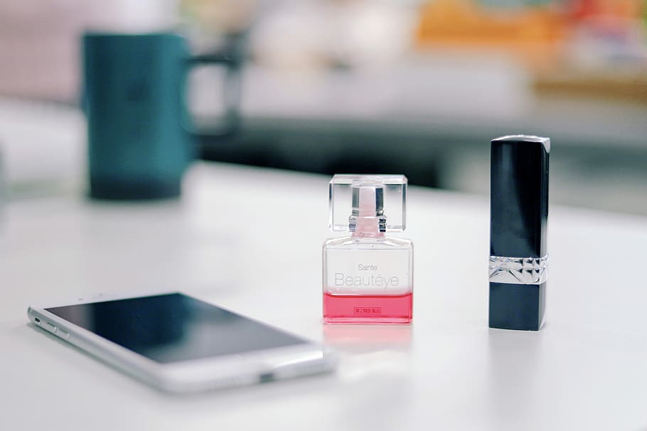smartphone on a table next to fragrance bottle and black lipstick bottle \, white smartphone beside glass perfume bottle and lipstick HD wallpaper