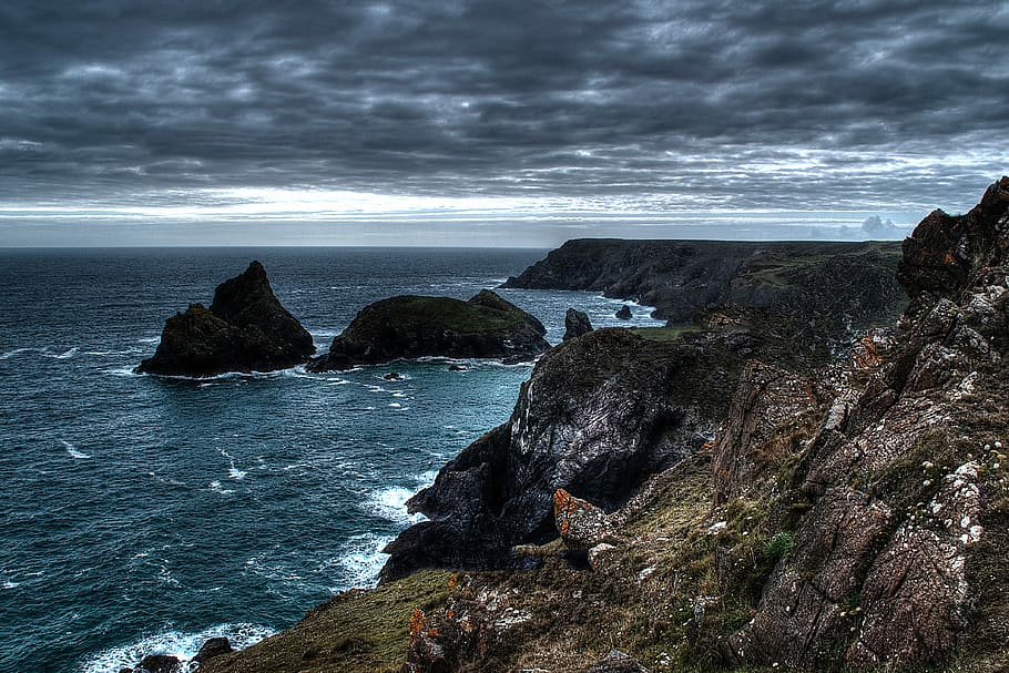 cliff beside body of water during cloudy day, rock formations on body of water under cloudy sky HD wallpaper