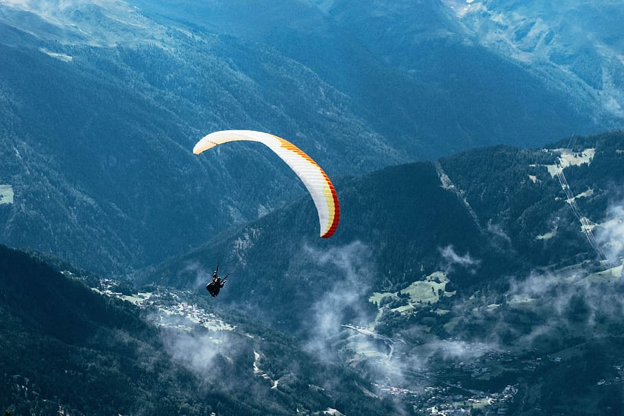 person paragliding over mountain ranges, person parachuting above green mountain during daytime HD wallpaper