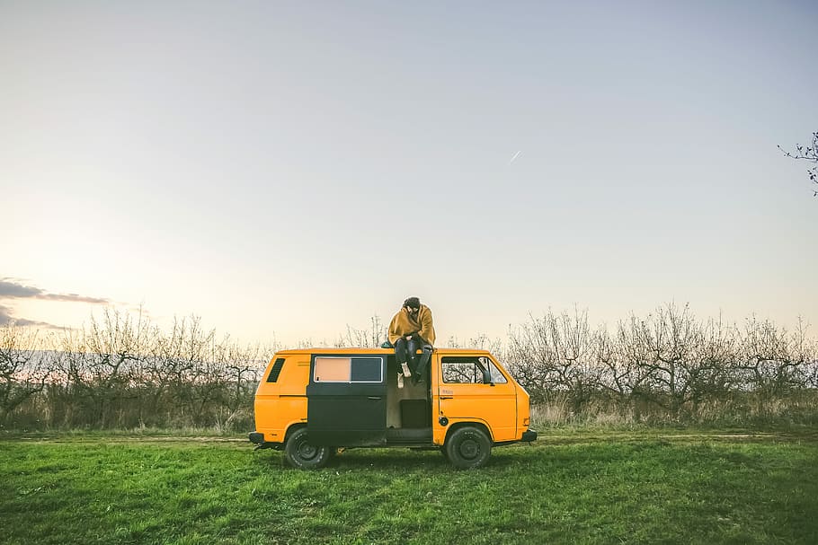 person sitting on top of yellow van on grass field during day, person on top of van