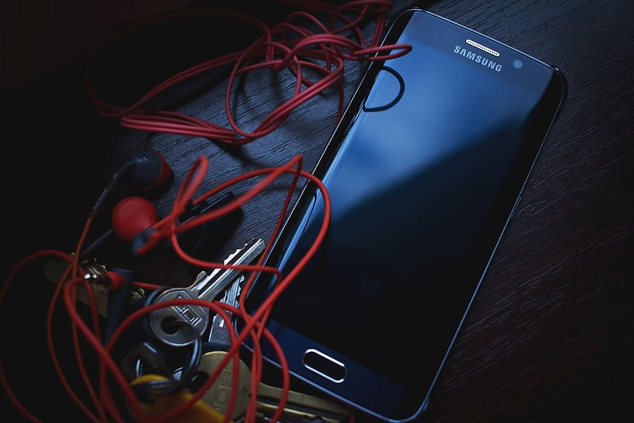 blue Samsung Android smartphone beside red earbuds and keys, cellphone