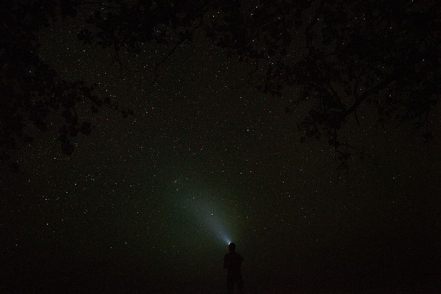 silhouette of person pointing his flashlight to the sky during nighttime photo, person standing under starry night sky HD wallpaper