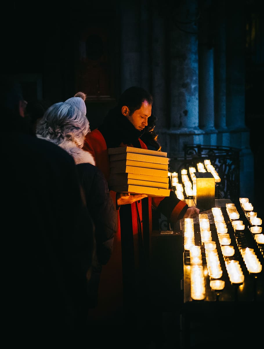 man in red coat holding white boxes holding candle, man standing near candles HD wallpaper