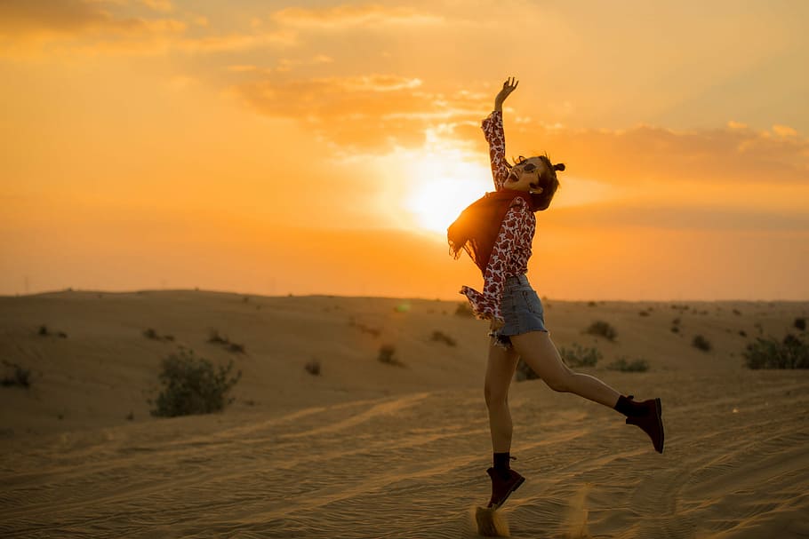 woman jumping on desert during golden hour, woman standing on rock during sunset HD wallpaper