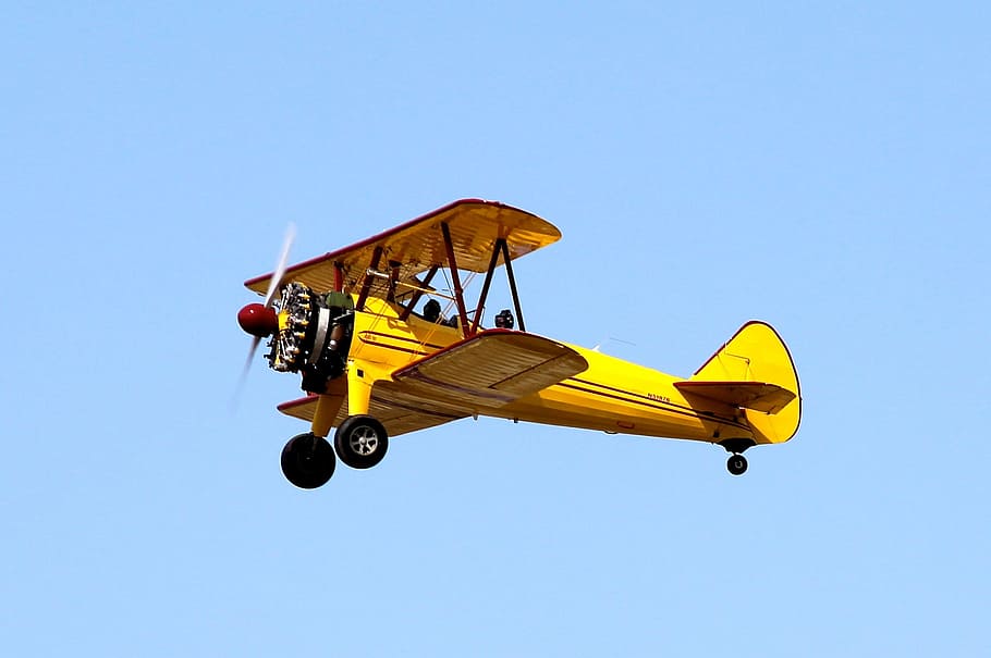 yellow biplane flying under clear blue sky view from ground during daytime HD wallpaper