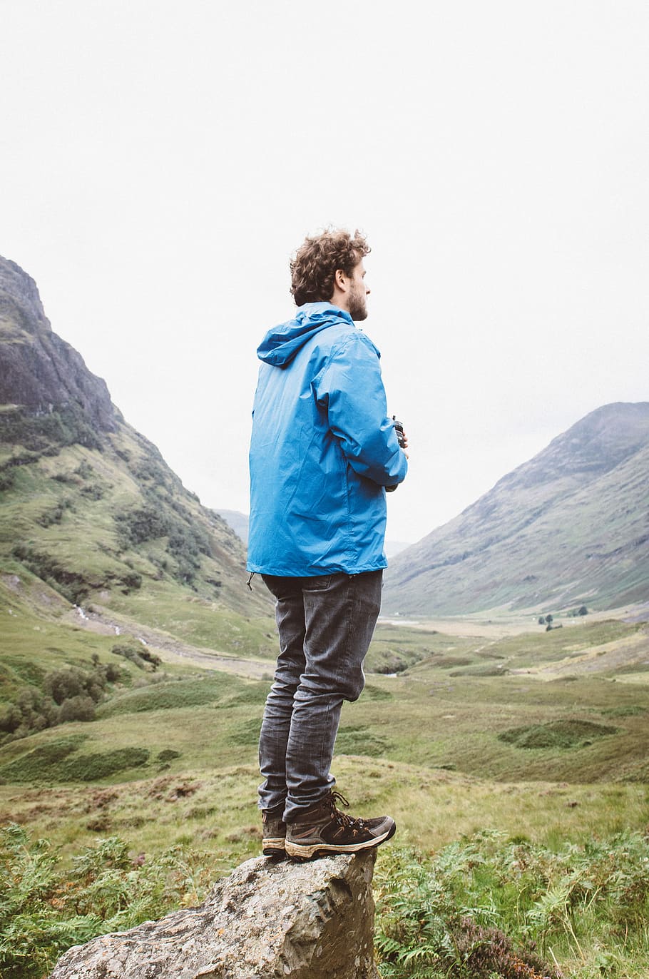 man standing on rock looking through mountain, man standing on cliff near mountains HD wallpaper
