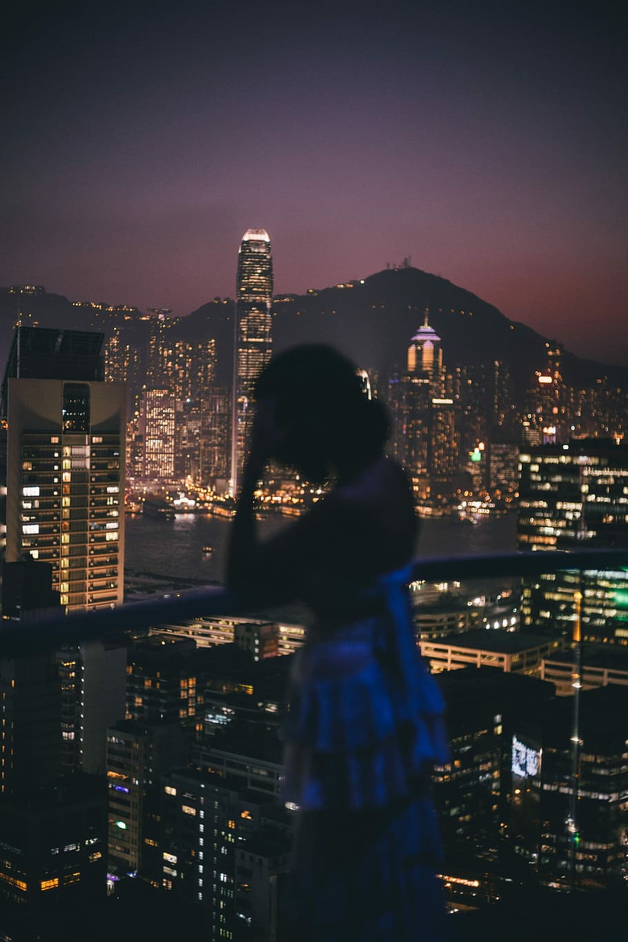 woman in backless top standing on veranda, woman leaning on rail with hand on forehead facing buildings during night time HD wallpaper