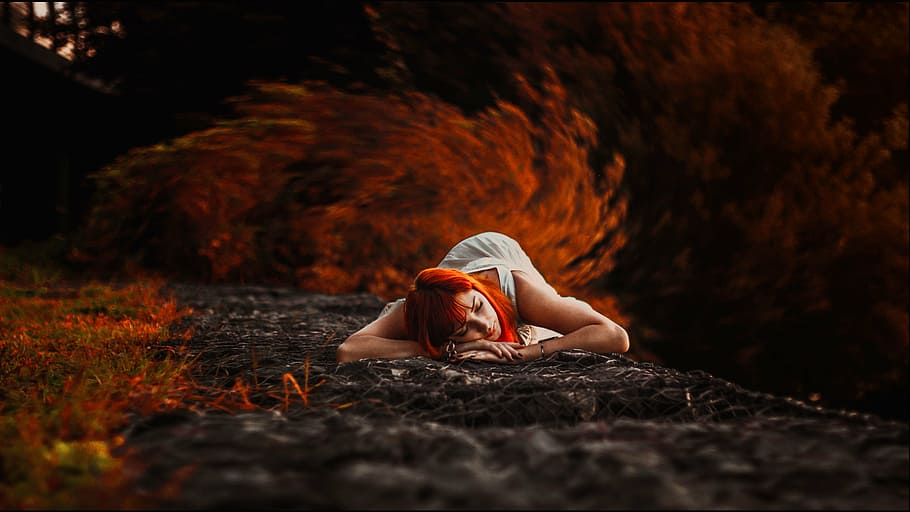 red-dyed haired woman in white dress lying on ground, autumn photoshoot