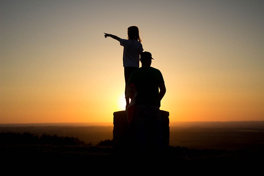 silhouette photo of two person sitting on cliff, silhouette photo of man and girl during golden hour
