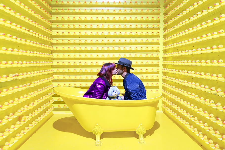 man and woman kissing inside yellow bathtub, woman wearing purple suit and man wearing blue suit kissing each other HD wallpaper