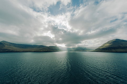 ocean under blue sky during daytime, body of water in distant of mountains HD wallpaper