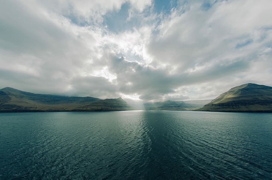 ocean under blue sky during daytime, body of water in distant of mountains HD wallpaper