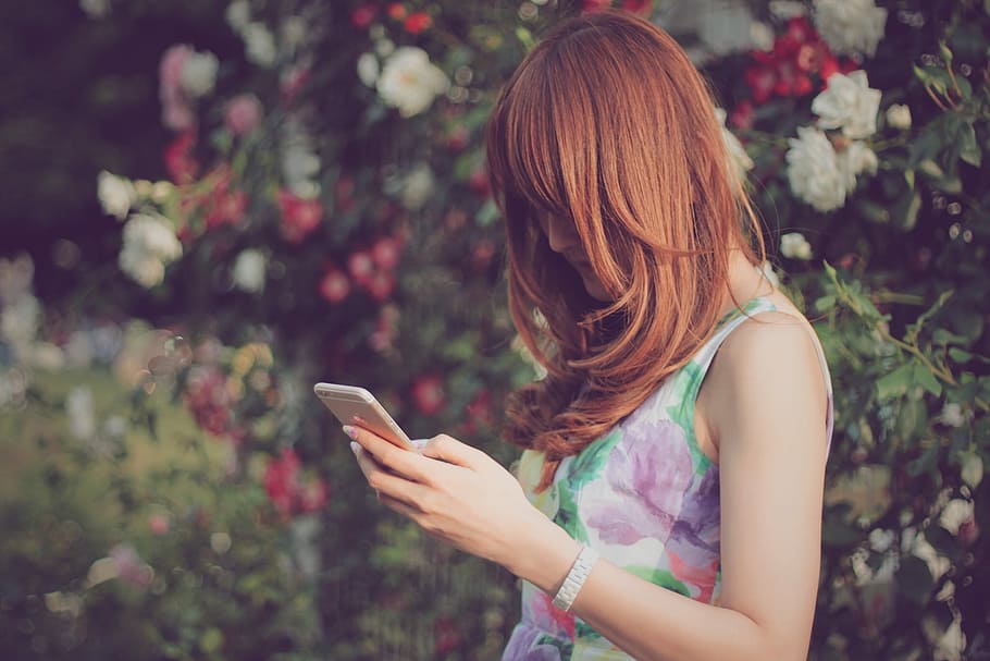 woman wearing floral sleeveless top holding gold iPhone 6, outdoors