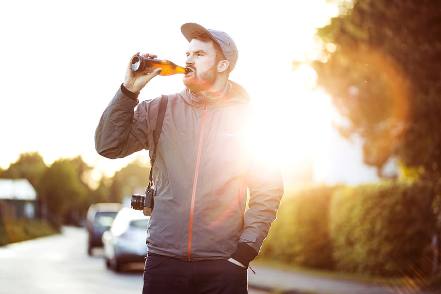man in gray and pink zip-up hoodie holding bottle while drinking during daytime, person drinking in bottle during daytime HD wallpaper