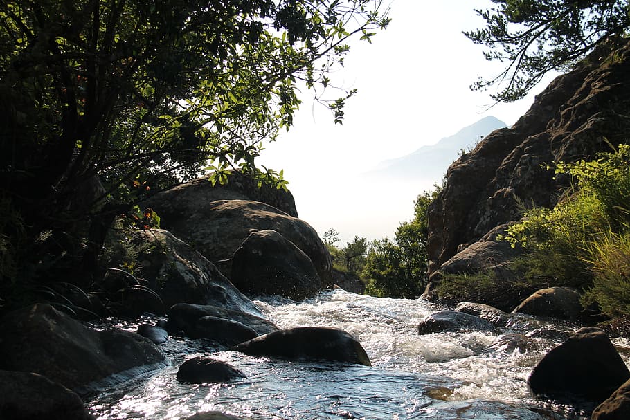 body of water between rock formation, brown rocky hills near body of water and green leafed trees during daytime HD wallpaper