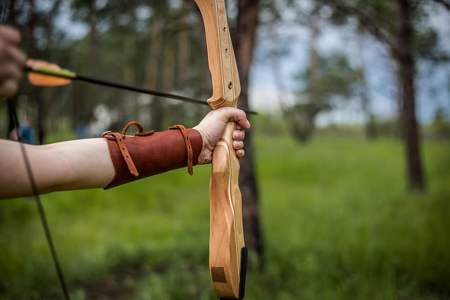 selective focus photo of person holding brown bow and arrow HD wallpaper