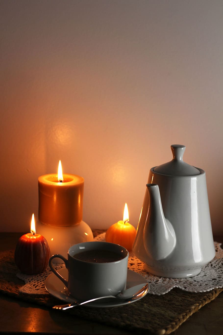 three orange candles beside teacup and teapot on brown mat, coffee