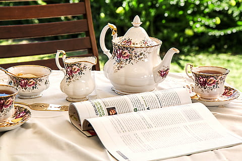 open magazine near white-and-pink floral tea set on top of table HD wallpaper
