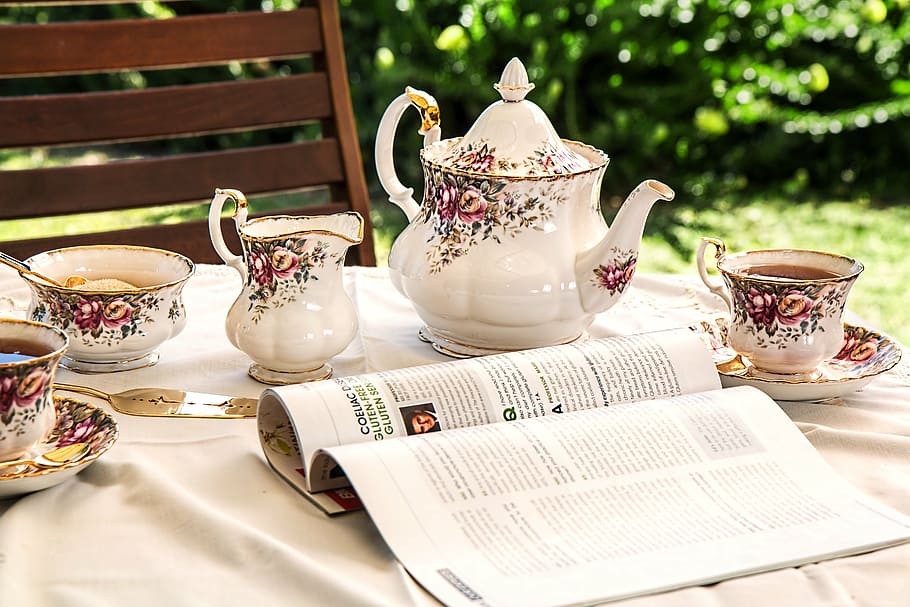 open magazine near white-and-pink floral tea set on top of table HD wallpaper
