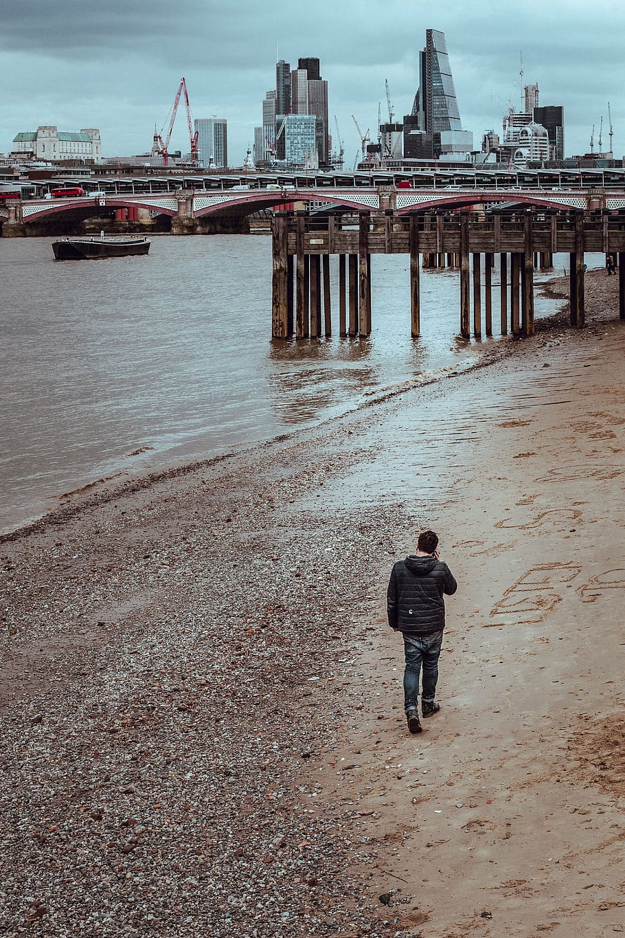 man walking on seashore towards brown wooden dock during daytime HD wallpaper