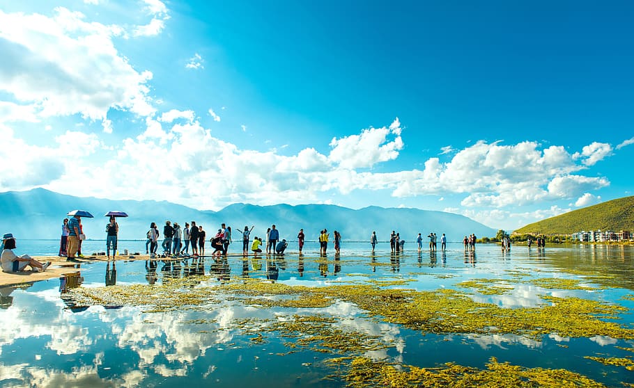 group of people standing on shallow body of water near mountains under cloudy blue sky