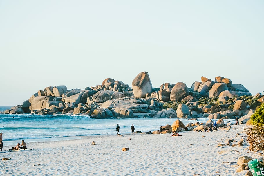 people walking on sand near beach, photo of people near shoreline and rock formations HD wallpaper