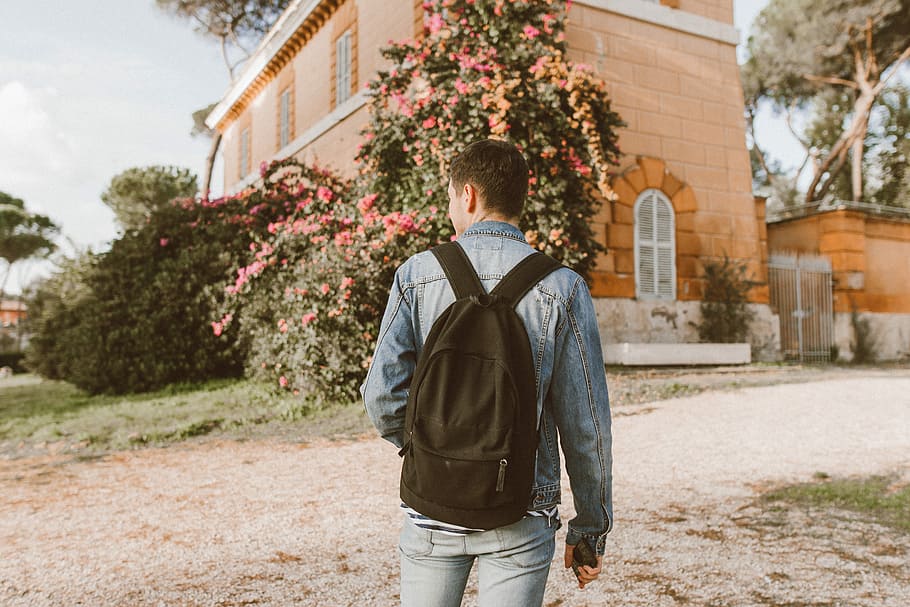 man with backpack standing in front of a house, man wearing black backpack walking HD wallpaper