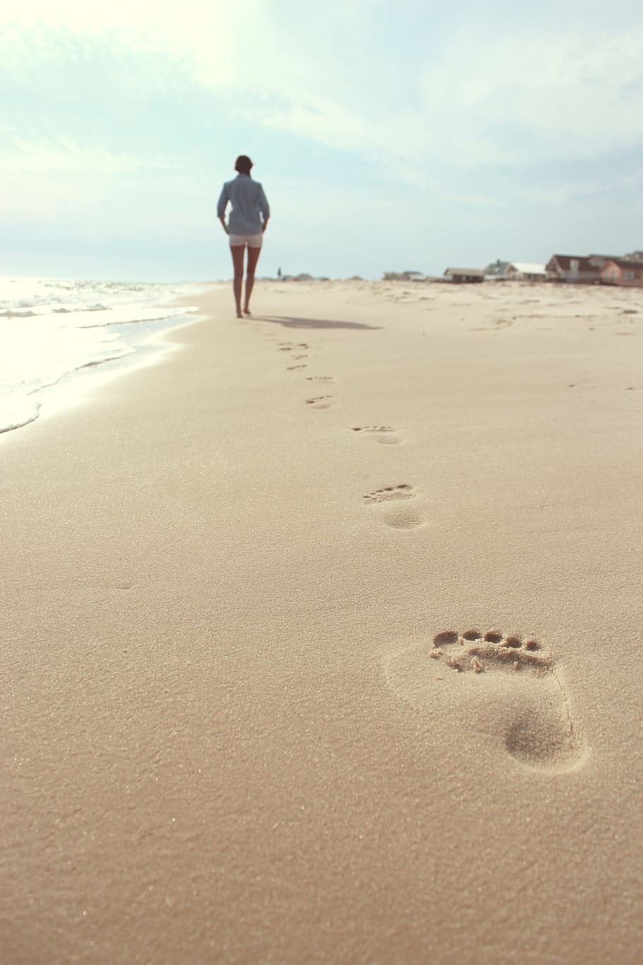 woman wearing blue dress shirt and white short shorts walking on seashore, person standing on seashore during daytime