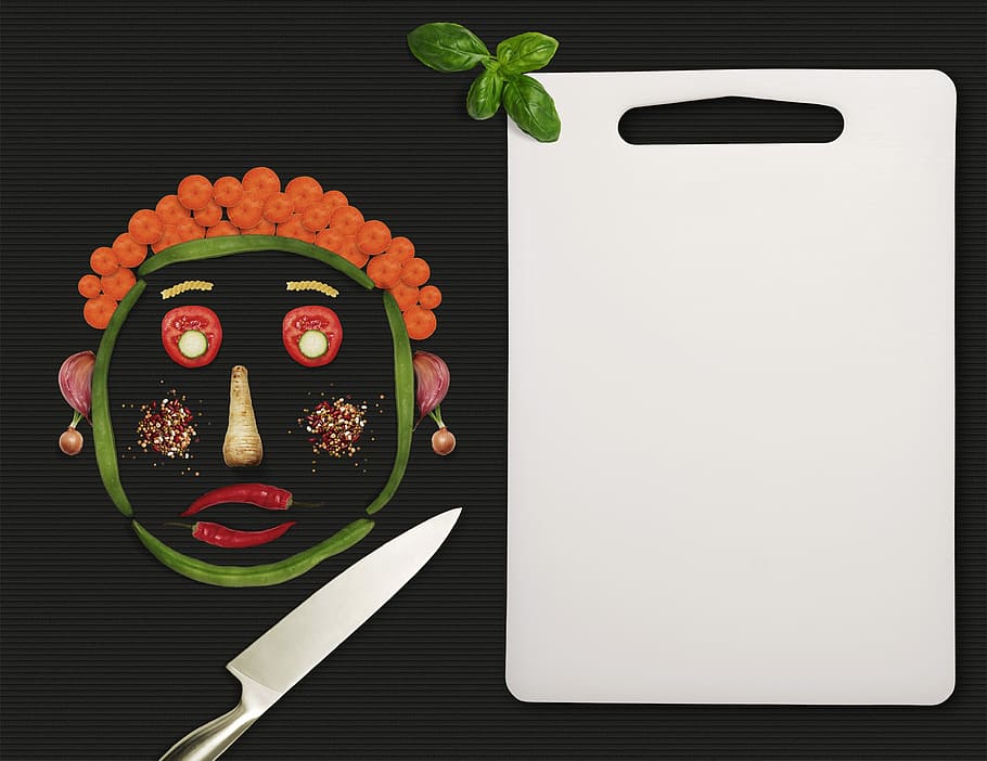 face-shaped sliced vegetables beside white chopping board and kitchen knife