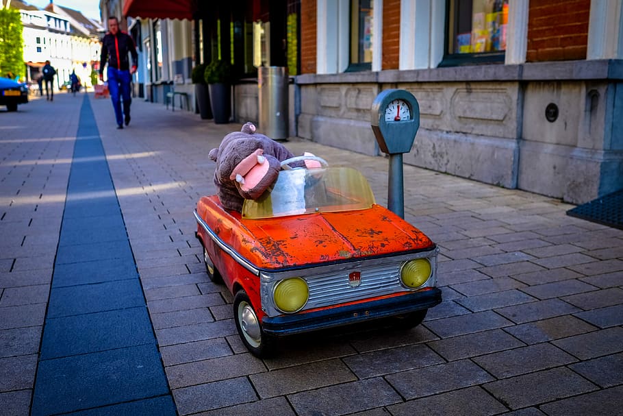 hippopotamus mascot riding red car toy beside the street, orange and gray ride-on toy parked near parkmeter HD wallpaper