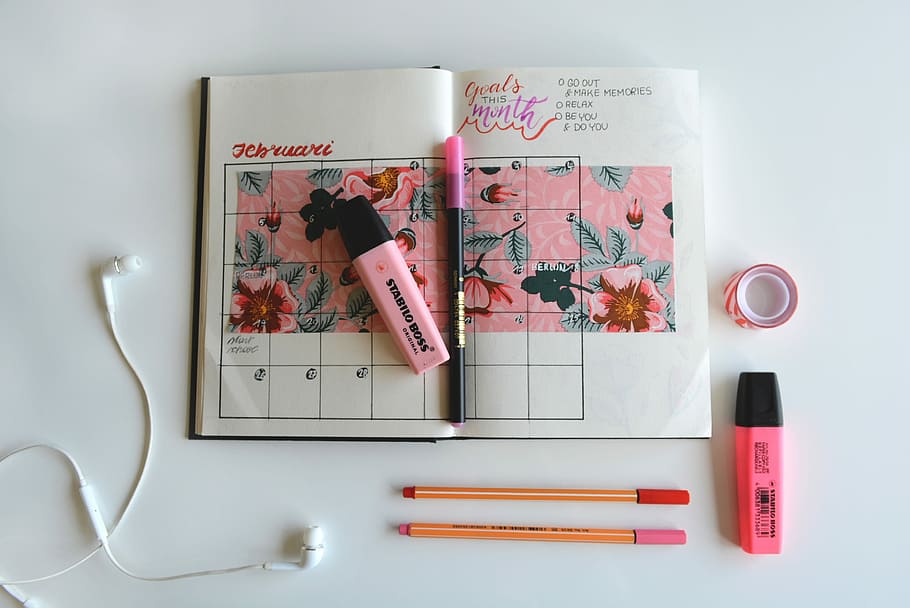 calendar notebook with highlighter pens, two red and pink highlighters on white surface HD wallpaper