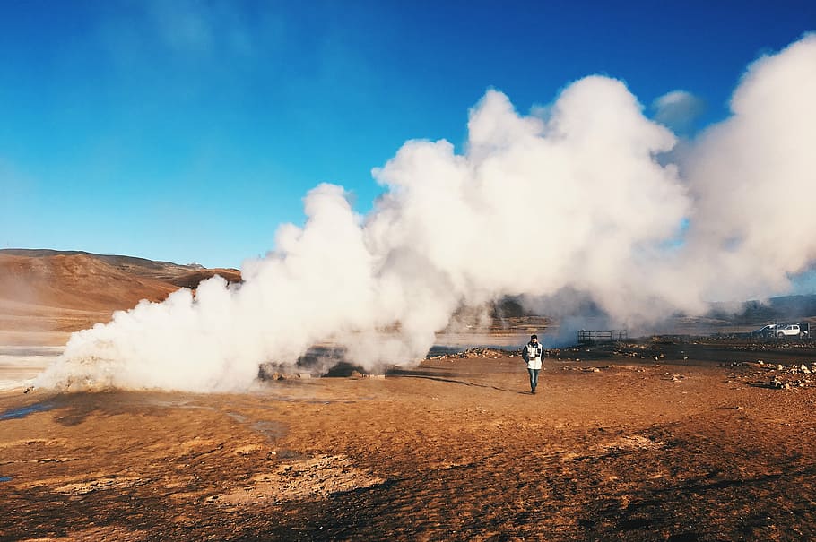 person stands near smoke under clear sky, man standing on brown mountain HD wallpaper