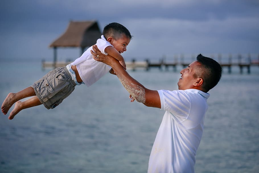 shallow focus photography of man carrying his son on beach during day time HD wallpaper
