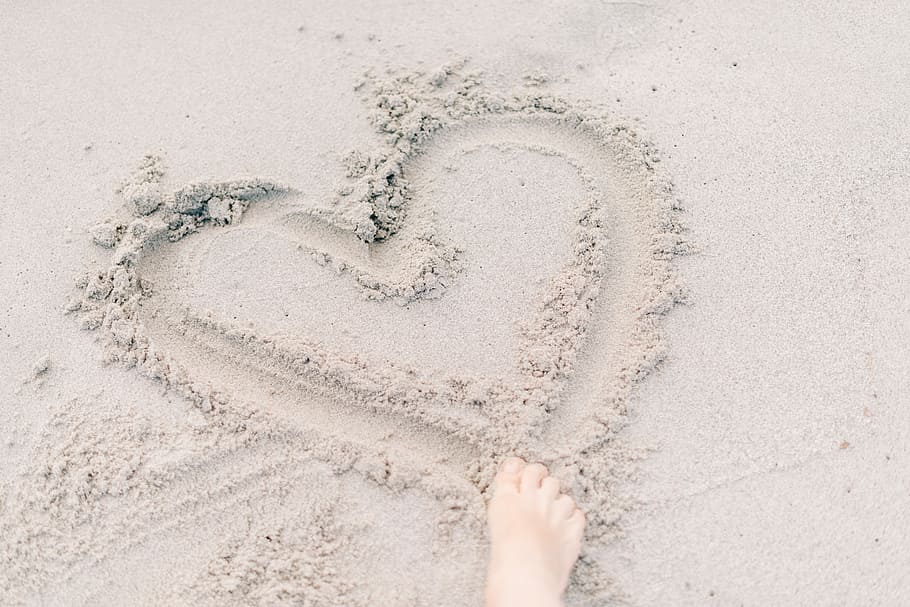 person forming heart on sand using right foot, person right foot on brown sand HD wallpaper