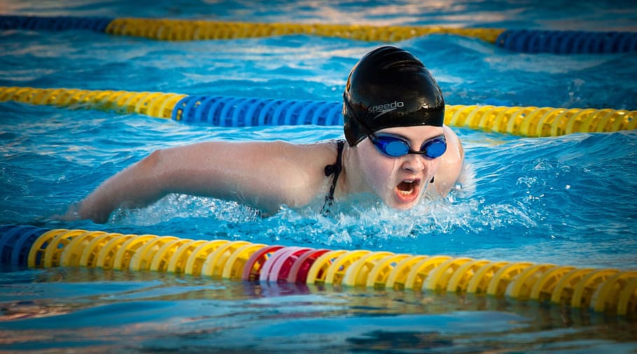 person wearing black swim cap and blue goggles, swimming, butterfly