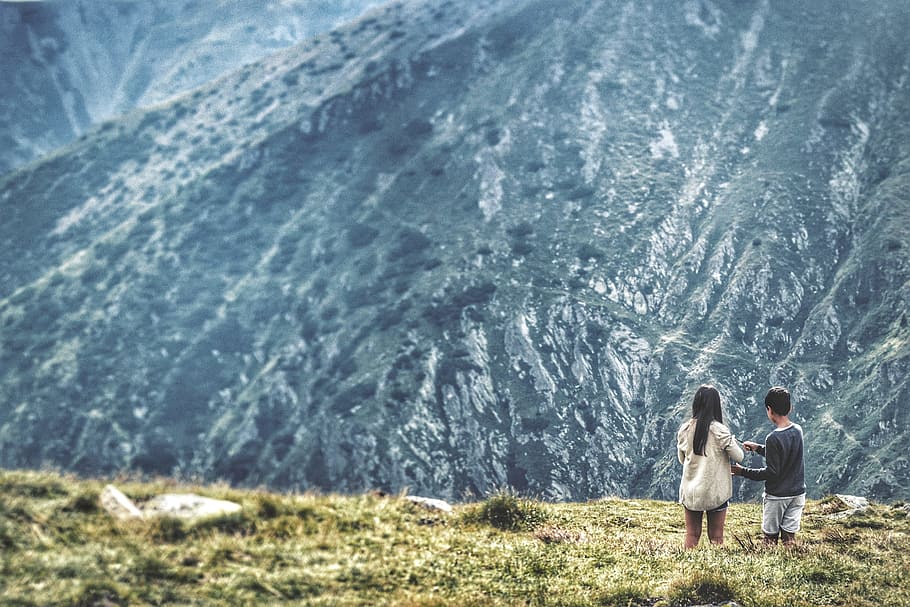 two people standing in front of mountains, man and woman on grass field HD wallpaper