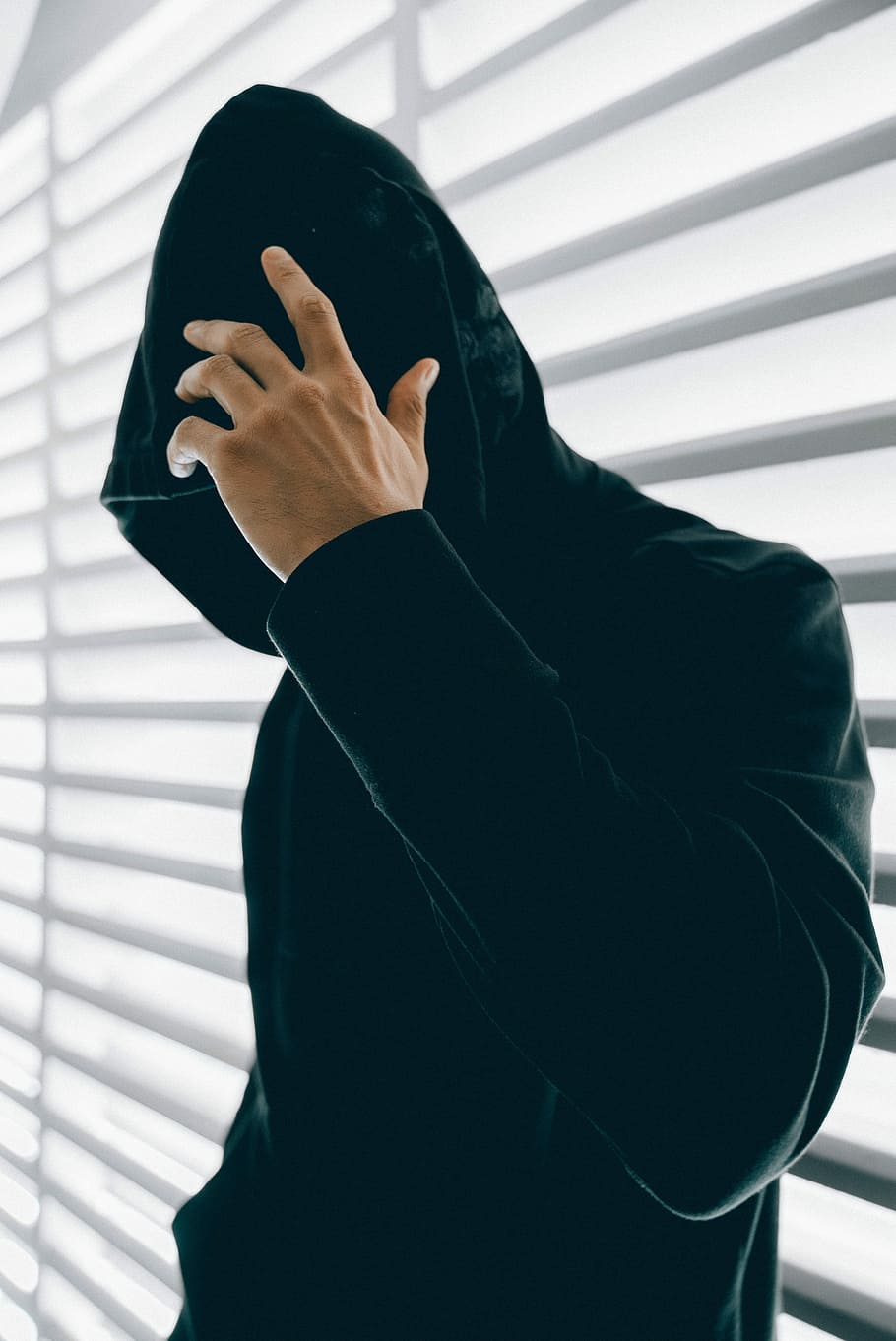 person wearing green hooded jacket inside room, man wearing black velvet hoodie standing beside window blinds