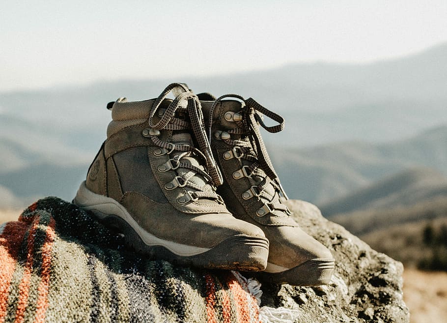 pair of brown high-top shoes on rock, pair of gray hiking shoes on rock