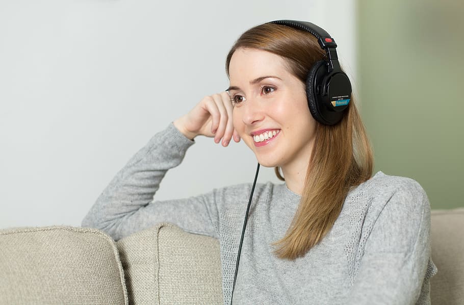woman wearing black corded headphones while sitting on sofa, girl
