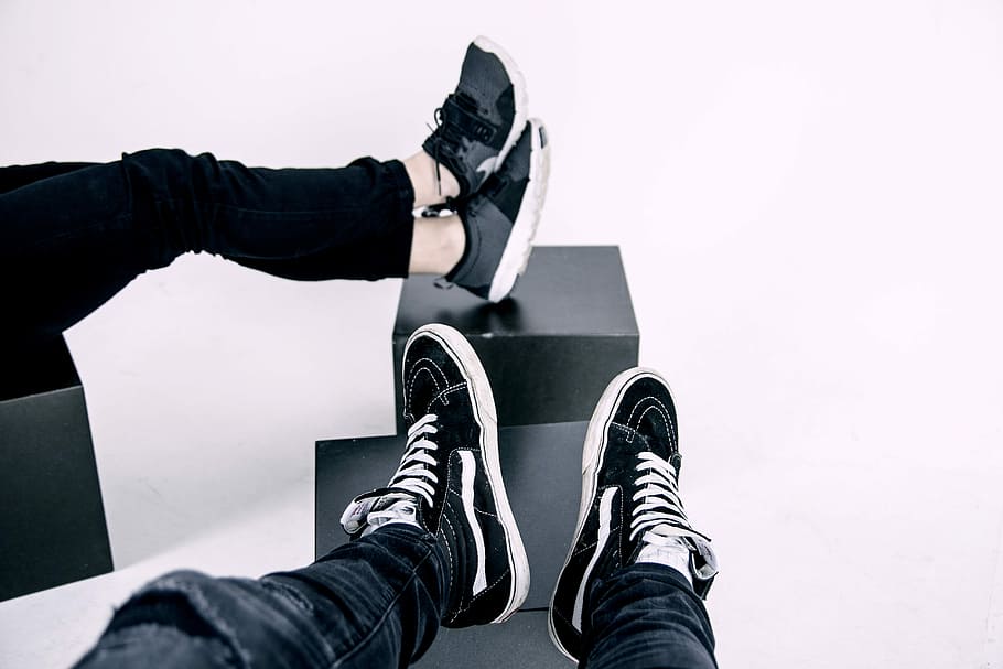 pair of white-and-black Vans high-top sneakers, two pairs of black sneakers on top of ottomans