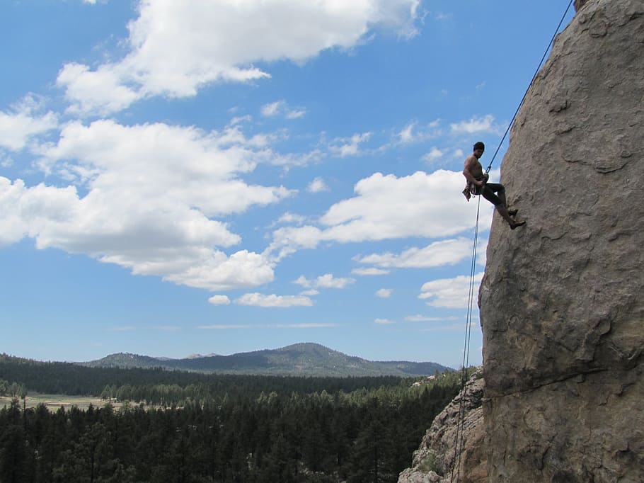 man rock climbing under white clouds and blue sky during daytime HD wallpaper