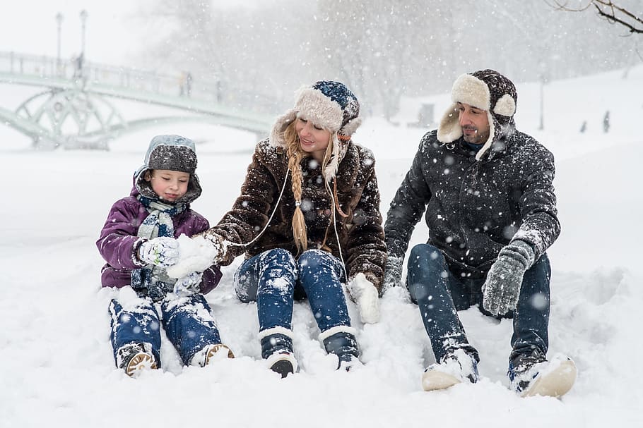 man, woman, and boy sitting on snow ground making snowballs, winter