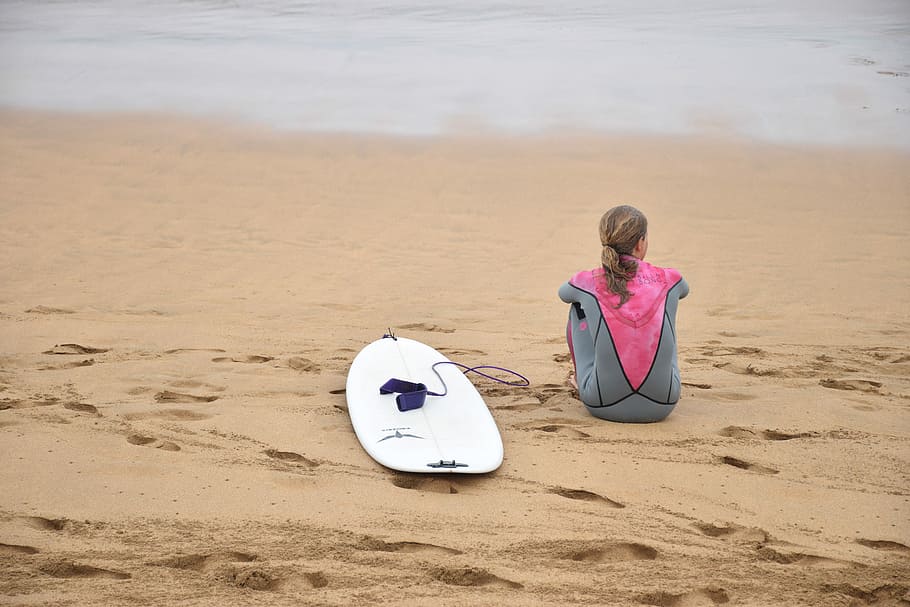 woman sitting on shore beside surfboard near sea, woman wearing pink wet suit and besides white surfboard, HD wallpaper