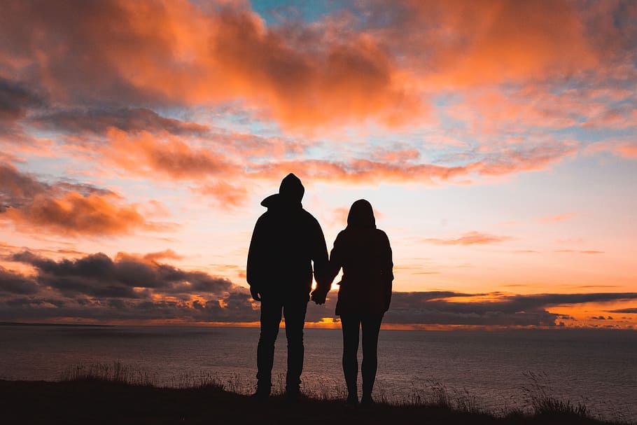 silhouette photo of man and woman on cliff, silhouette of man and woman holding hands facing sea at sunset