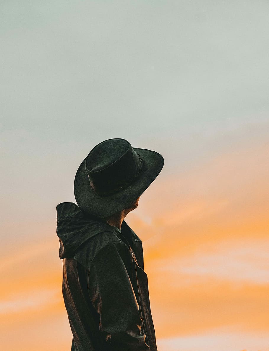 close-up photography of man wears black cowboy hat while looking up, man wearing black jacket and hat facing sun HD wallpaper