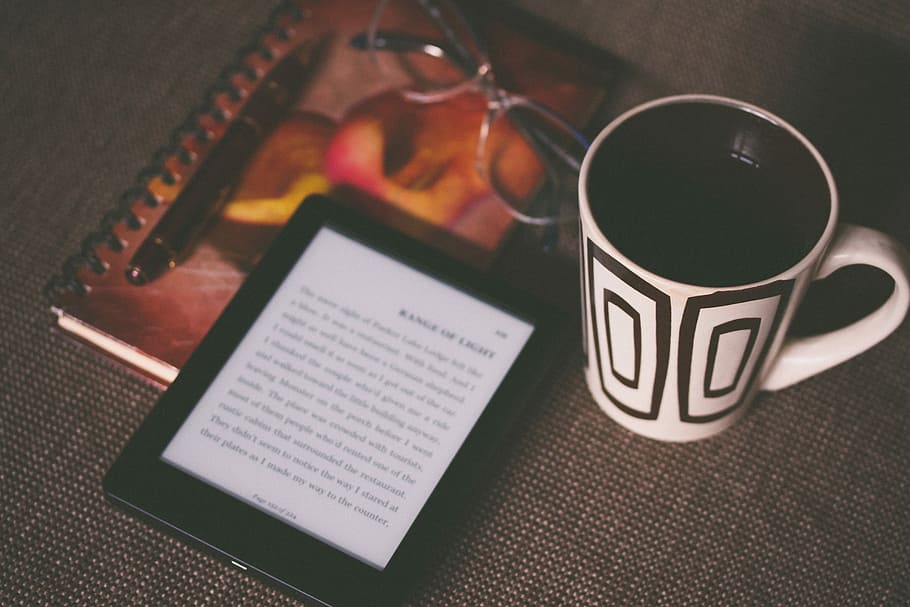 black E-book reader beside white and black mug, black tablet computer beside coffee cup