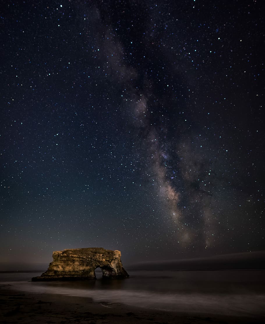 brown rock formation on body of water during nighttime, rock monolith during nighttime with shining stars
